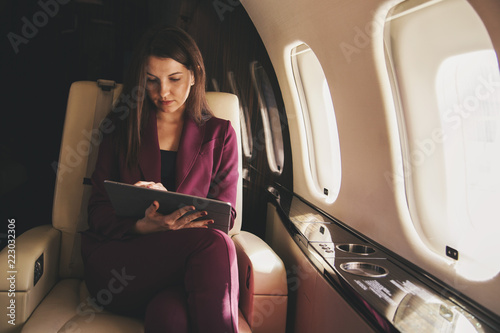 beautiful young woman sits in a plane and works on laptop