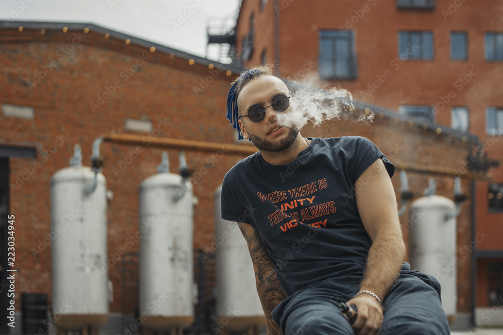 Portrait of young vaping man with dreadlocks. Vapor concept. Vaping e-Cigarette Portrait of young vaping man with dreadlocks. Vapor concept. Vaping e-Cigarette