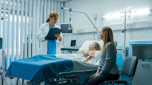 Sick Little Girl Lies on a Bed In the Hospital, Friendly Doctor With Clipboard Asks Where it Hurts, Mother Sits Beside Bed. Cute Child is Taken Care of in the Modern Pediatric/ Children Ward.