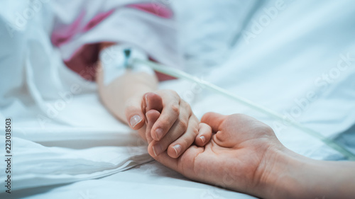 Fotografiet Recovering Little Child Lying in the Hospital Bed Sleeping, Mother Holds Her Hand Comforting
