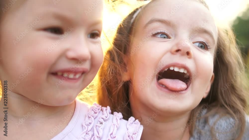 Babies, two little sisters fool around, show the tongue and make faces. children walk in the garden, active way of life, happy holidays