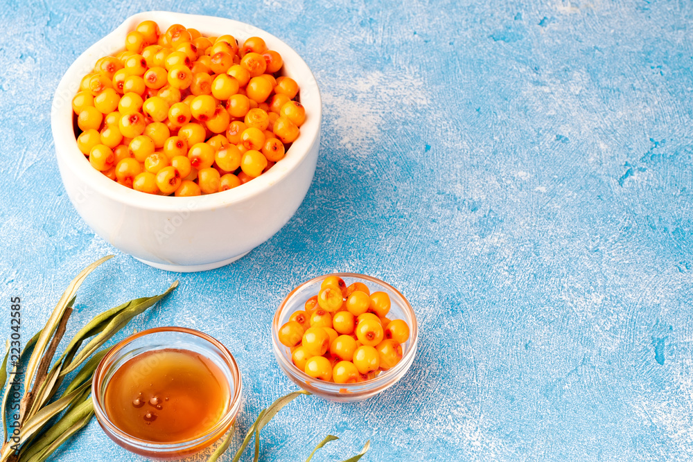 Sea-buckthorn berries in bowl and natural honey or sea buckthorn oil on blue background Sea-buckthorn berries in bowl and natural honey or sea buckthorn oil on blue background