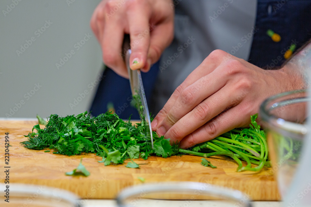 Human hands with sharp steel knife shredding green parsley leaves on wooden board for salad or stew