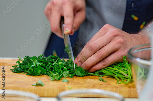 Human hands with sharp steel knife shredding green parsley leaves on wooden board for salad or stew