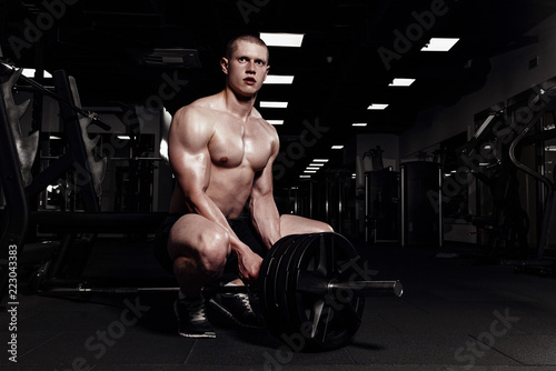 Muscular strong athletic men pumping up muscles and training in gym. Handsome bodybuilder guy doing exercises with barbell.