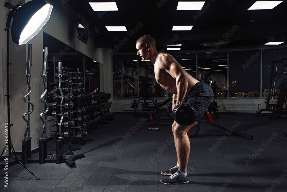 Athletic young man doing exercises with barbell in gym. Handsome muscular bodybuilder guy is working out. Backstage. Athletic young man doing exercises with barbell in gym. Handsome muscular bodybuilder guy is working out. Backstage.