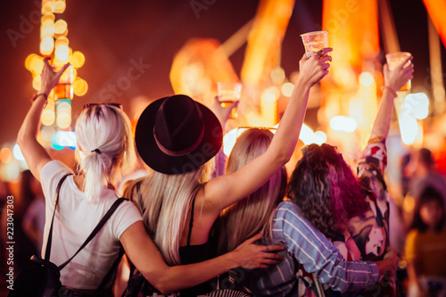 Photo Back view of group of female friends at music festival drinking beer and dancing