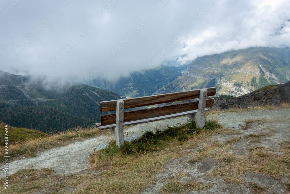 Wooden bench with beautiful mountain landscape with fog and clouds near the Matterhorn