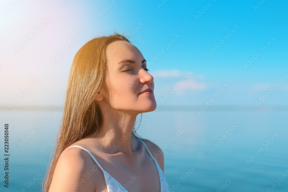 Close - up of a young brunette breathes clean sea air on the background of clear sky and sea, fresh air, freedom, ecology Close - up of a young brunette breathes clean sea air on the background of clear sky and sea, fresh air, freedom, ecology