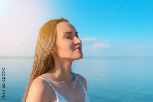 Close - up of a young brunette breathes clean sea air on the background of clear sky and sea, fresh air, freedom, ecology