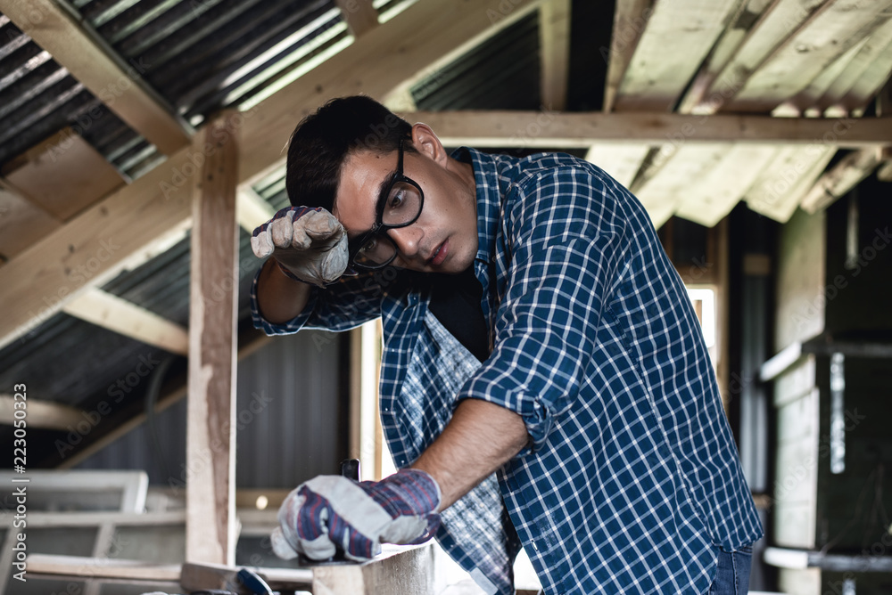 Man in goggles and wipes his forehead from sweat when handling wooden boards planer, heavy manual labor, handyman