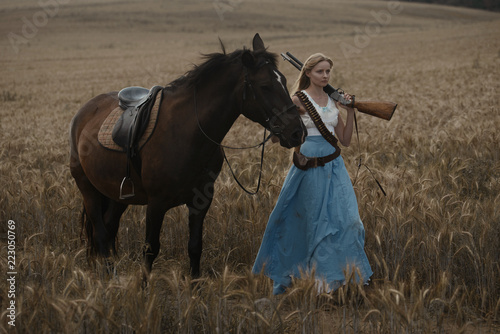 Obraz na plátně Portrait of a beautiful female cowgirl with shotgun from wild west riding a horse in the outback