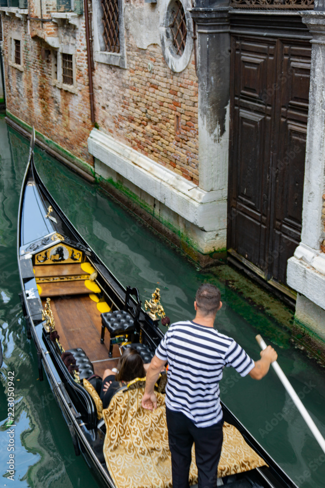 Venetian gondolier punting gondola through narrow canal waters of Venice, Veneto, Italy