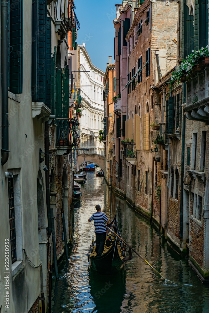 Venetian gondolier punting gondola through narrow canal waters of Venice, Veneto, Italy
