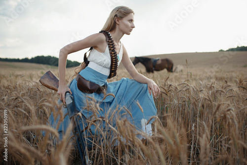Portrait of a beautiful female cowgirl with shotgun from wild west riding a horse in the outback.