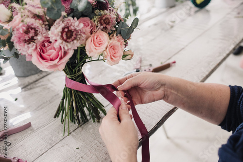 hands of a florist bandage a bouquet with a pink ribbon photo