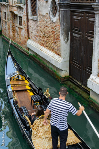 Venetian gondolier punting gondola through narrow canal waters of Venice, Veneto, Italy