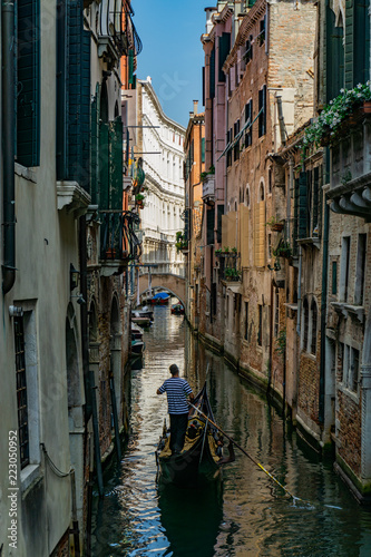 Venetian gondolier punting gondola through narrow canal waters of Venice, Veneto, Italy