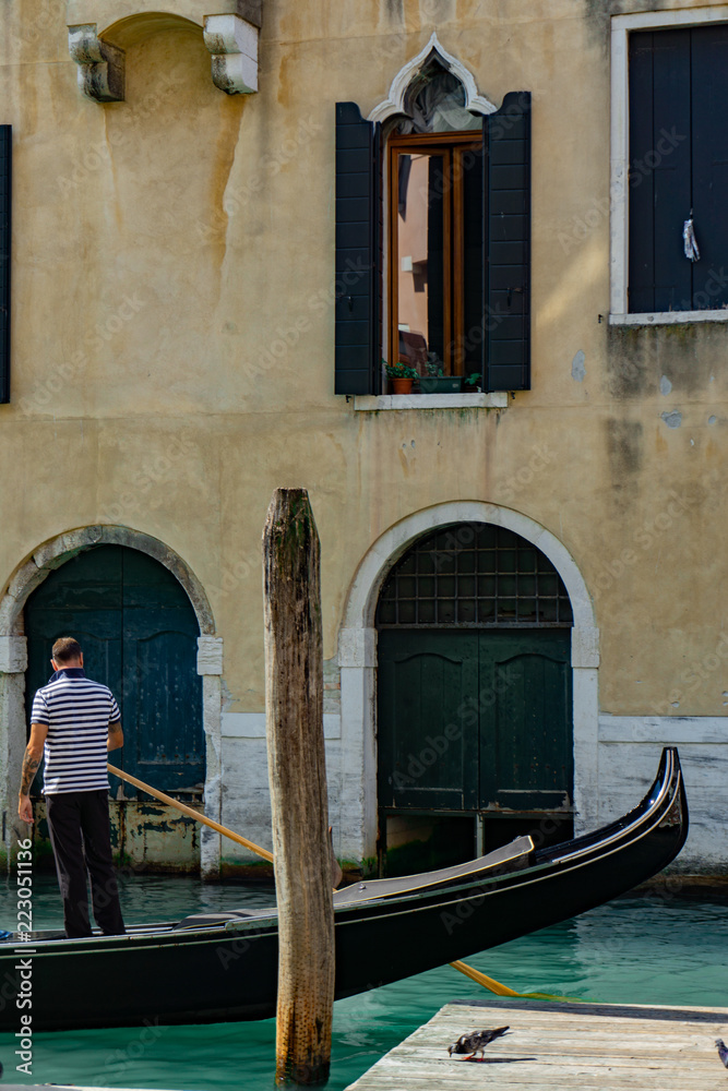 Venetian gondolier punting gondola through narrow canal waters of Venice, Veneto, Italy