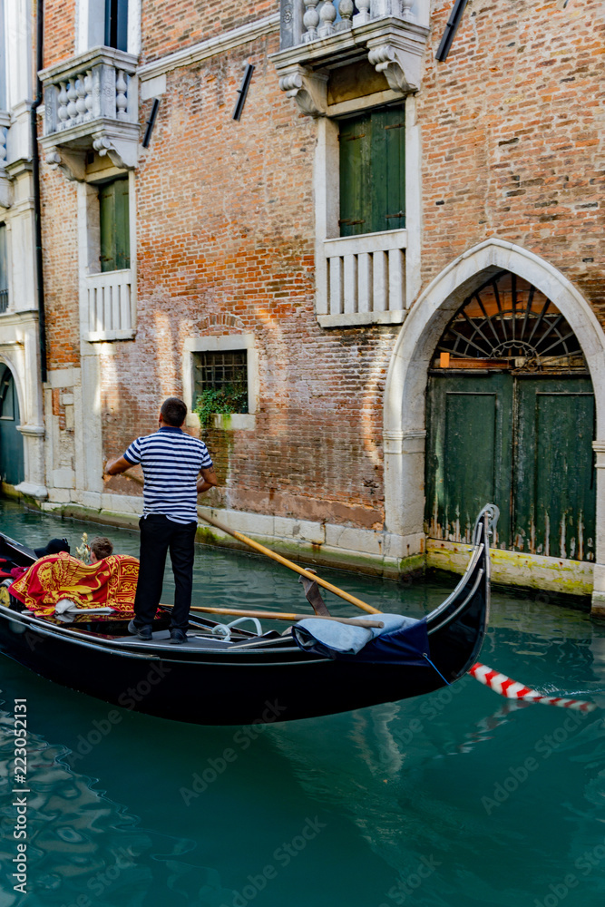 Venetian gondolier punting gondola through narrow canal waters of Venice, Veneto, Italy
