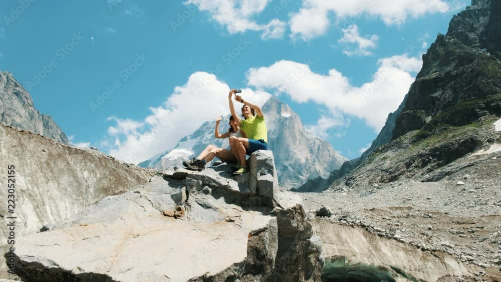 Loving family young couple of tourists sit on a rock and take pictures and shoot video on a smartphone Loving family young couple of tourists sit on a rock and take pictures and shoot video on a smartphone