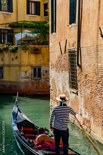 Venetian gondolier punting gondola through narrow canal waters of Venice, Veneto, Italy © marcodotto