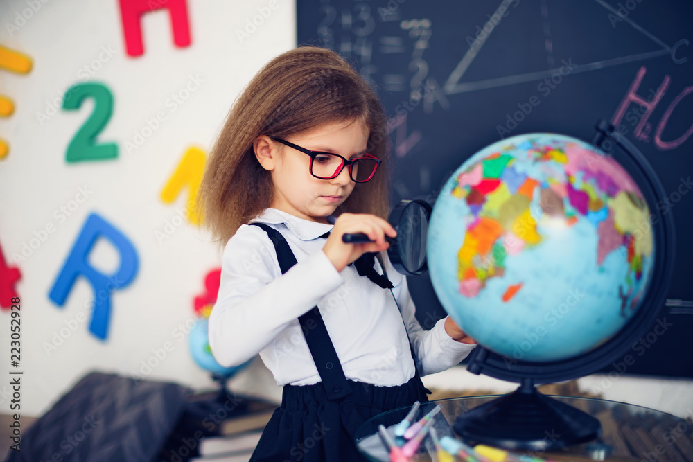 Fototapeta premium Portrait of a beautiful young schoolgirl girl exploring the globe through a magnifier. day of knowledge. beginning of the school year. studying geography with globe