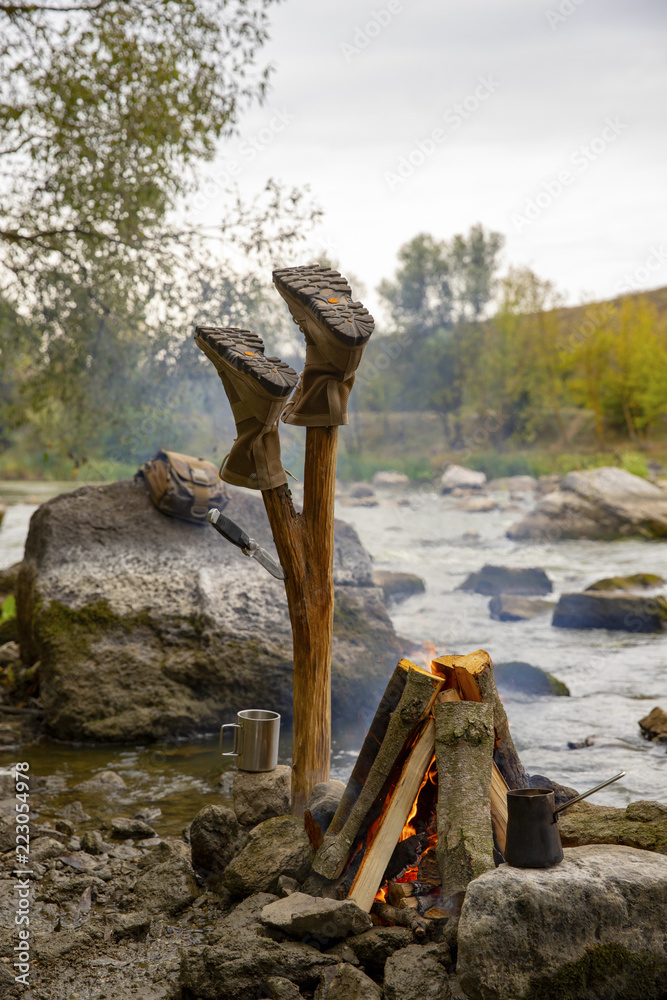 The shoes are dried. Military boots. Tourist shoes. A tourist camp on the river bank. Stop by the river bank. Tourist equipment. A man is warmed by the fire. The shoes are dried. Military boots. Tourist shoes. A tourist camp on the river bank. Stop by the river bank. Tourist equipment. A man is warmed by the fire.