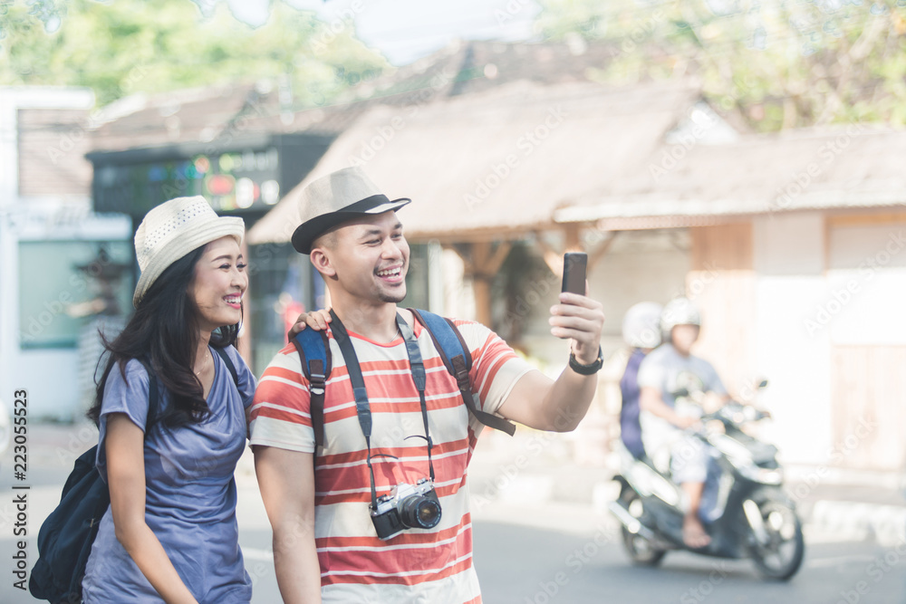 Naklejka premium two young backpackers taking selfies using mobilephones camera