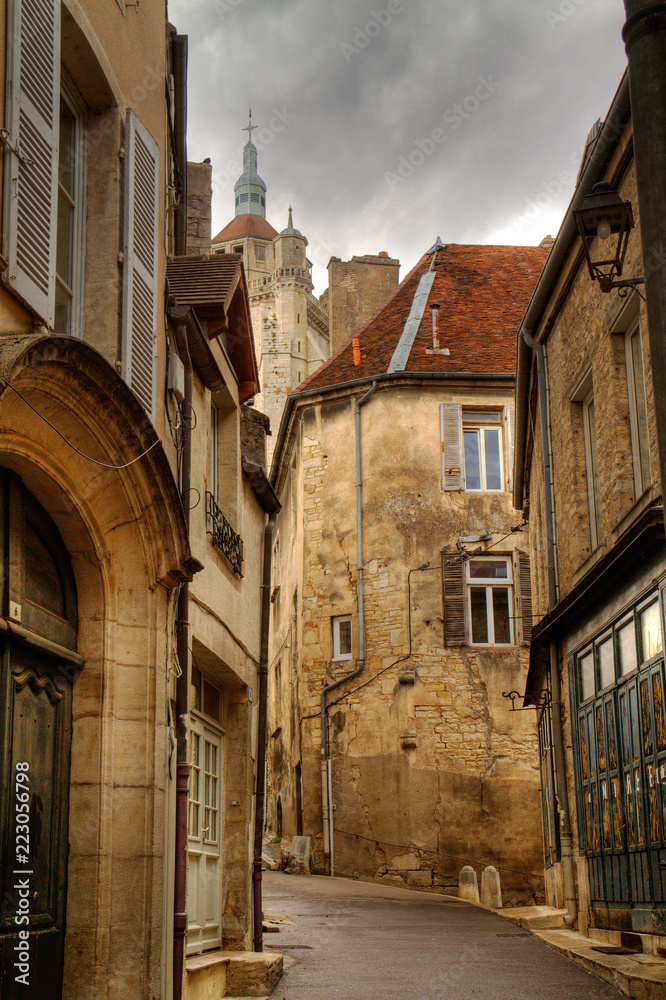 Narrow street in the beautiful old French town Dole, the steeple of the church of Notre-Dame and dark clouds above the old houses