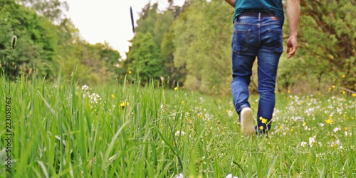 Close-up on the feet - man is walking in the summer through a green meadow