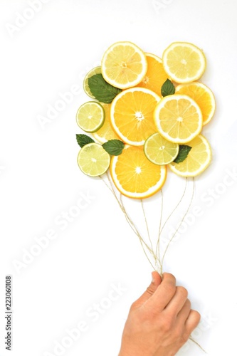 Close-up - A young man's hand holds strings at the end of which citrus fruits such as orange, lemon and lime float away as balloons - concept with citrus fruits as balloons