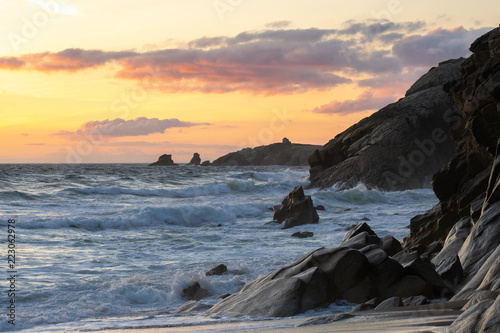 Des grosses vagues viennent frapper les falaises sous les couleurs oranges d'un coucher de soleil  photo