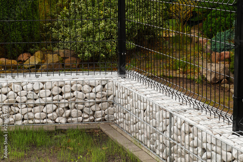 Gabion. A steel fence combined with a low wall made of gabions filled with white pebbles.
