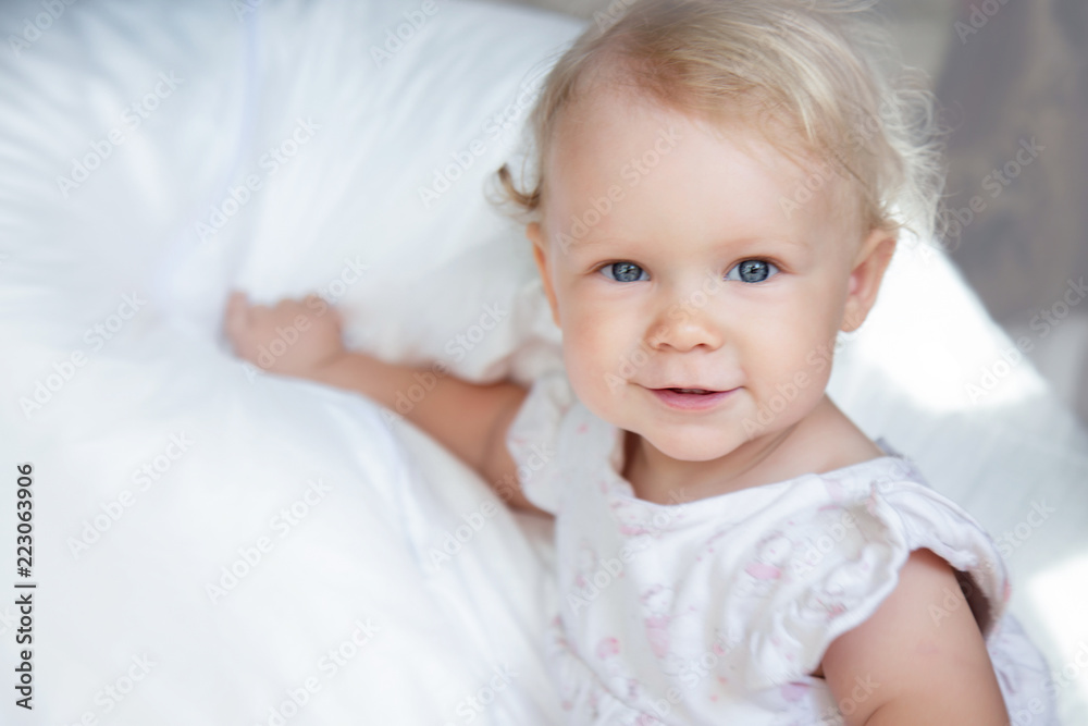 Close up portrait of a cute baby girl with big beautiful blue eyes and with blonde curly hair relaxing on a white blanket. Little girl 1 year old Stock Photo | Adobe Stock Close up portrait of a cute baby girl with big beautiful blue eyes and with blonde curly hair relaxing on a white blanket. Little girl 1 year old Stock Photo | Adobe Stock