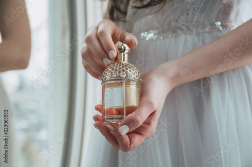 A girl in a white dress holds a bottle with perfume.