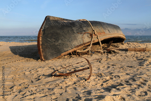 Obraz na płótnie A black fishing boat lies upside down with a keel on a sandy beach