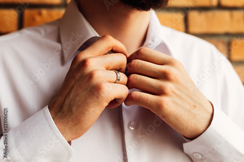 A close-up of the groom that fastens the buttons on a white shirt