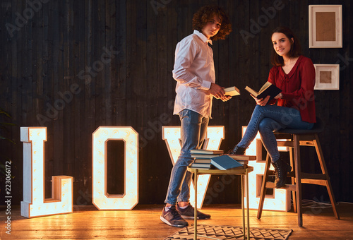 Young student couple reading together in a room decorated with voluminous letters with illumination.