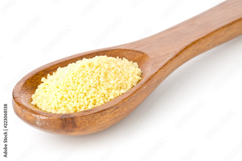 Heap of raw, uncooked couscous in wooden spoon over white Heap of raw, uncooked couscous in wooden spoon over white