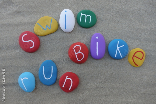 Swim, run, bike, three sports of triathlon, text words with colored stones over beach sand