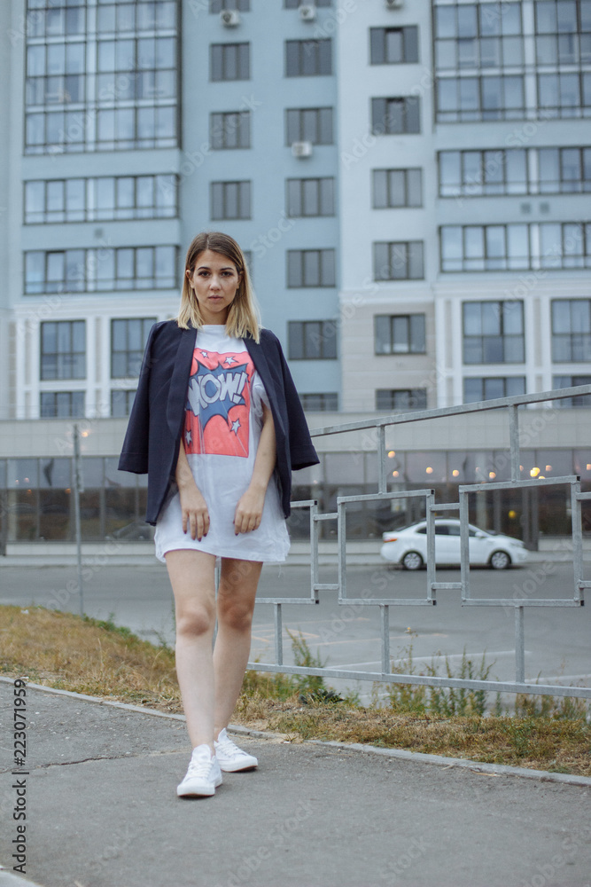 Fototapeta premium Beautiful woman with nude legs walking around city street wearing long white shirt