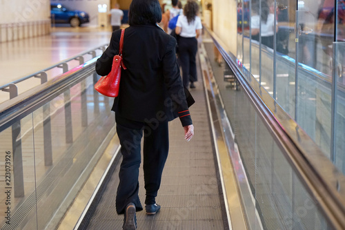 Woman at horizontal escalator covered. Moving walkway, moving sidewalk, moving pavement, autopedescalator, walkalator, travelator, autowalk, horizontal escalator, slidewalk, or moveator at an airport.