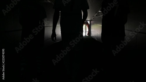 Three football players are walking along a dark tunnel to the football field. View from the back