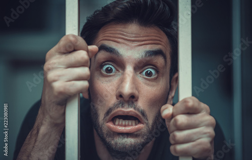 Solitude concept, man behind prison or cage bars trying to break free, mentally ill and deranged
