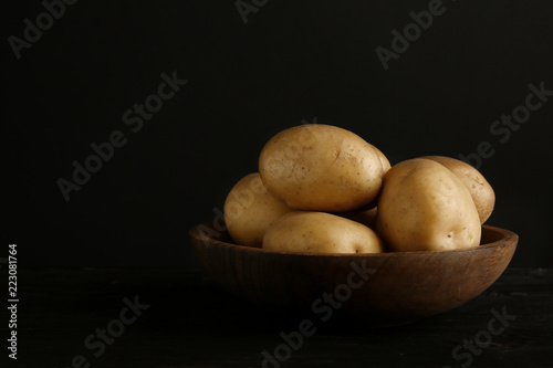 Fresh organic potatoes in bowl and space for text on black background