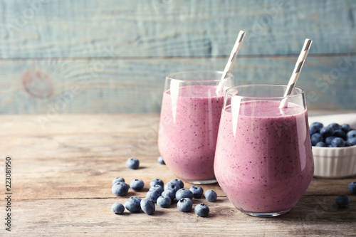 Tasty blueberry smoothie in glasses and berries on wooden table against color background with space for text