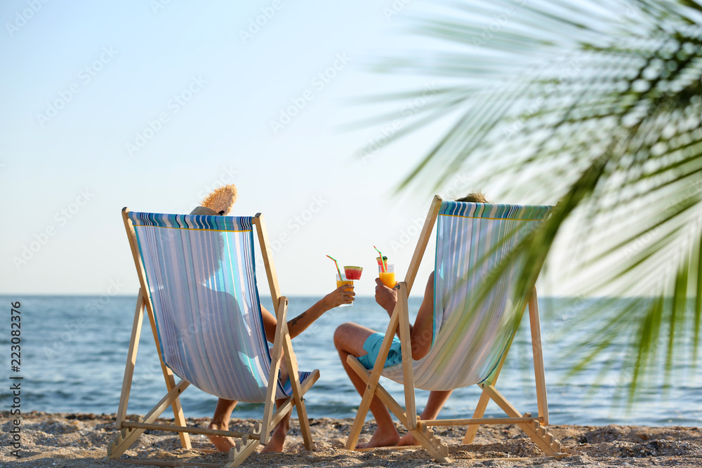 Naklejka premium Young couple with cocktails in beach chairs at seacoast