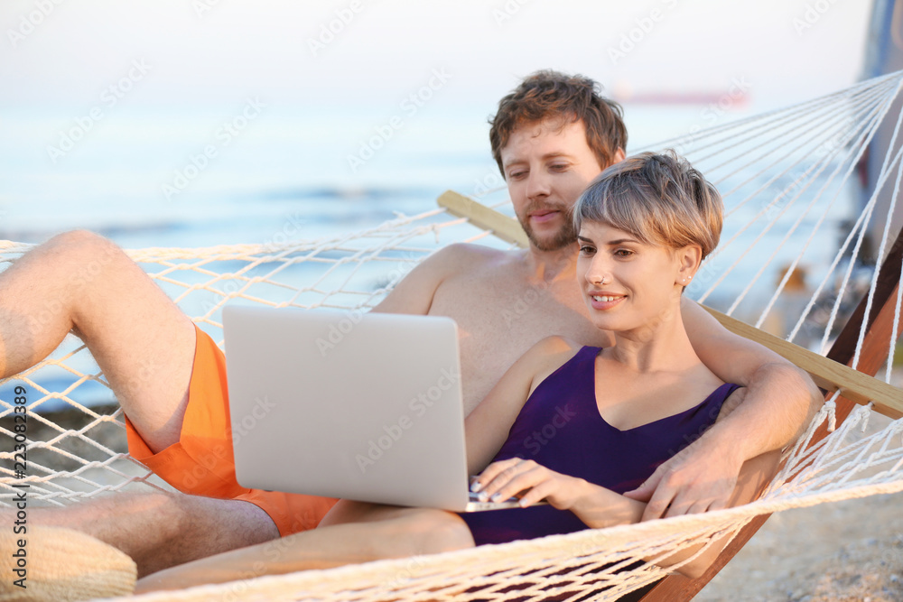 Young couple resting with laptop in hammock on beach Young couple resting with laptop in hammock on beach