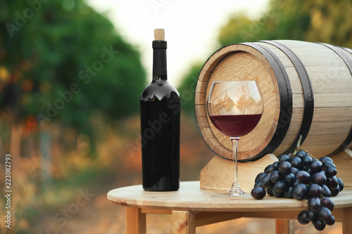 Fototapeta Naklejka Na Ścianę i Meble -  Bottle of wine, barrel and glass on wooden table in vineyard